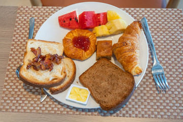 Plate of ham bread butter with fruits and croissant