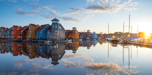 Tranquil dawn at colorful wooden houses in a small harbor in the Netherlands.  Living at the waterfront in Groningen. - obrazy, fototapety, plakaty