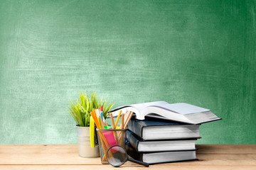 Pile of books with potted plant and pencils in basket container with magnifying glass on the wooden table