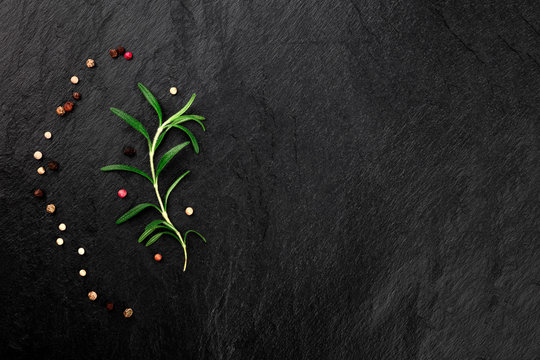 A rosemary branch with pepper, shot from the top on a black background with copy space