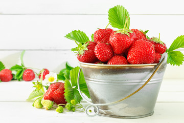 Juicy ripe tasty strawberries in  metal bucket on white wooden table.