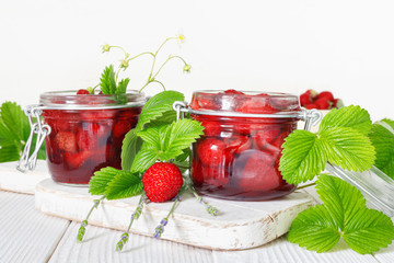 Delicious strawberry jam in traditional glass jar on white wooden background