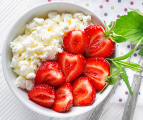 White bowl with fresh red ripe strawberries and natural cottage cheese