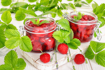 Delicious strawberry jam in traditional glass jar on white wooden background