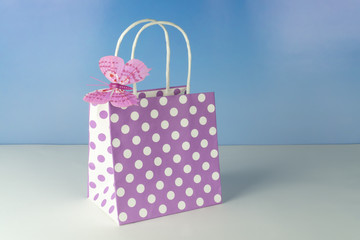 Purple gift bag with white dots and a butterfly, blue background
