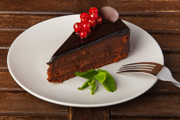 Chocolate cake plate. Decoration of fresh red currant berries, mint and chocolate pieces. Cake on a plate on a wooden table.