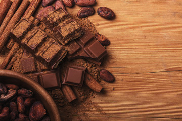 Chocolate pieses with cocoa powder and cocoa grains on wooden background