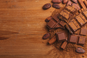 Chocolate pieses with cocoa powder and cocoa grains on wooden background