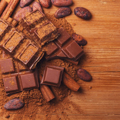 Chocolate pieses with cocoa powder and cocoa grains on wooden background