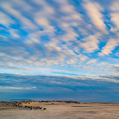 Square frame Boundless blue sky with gray and white clouds over a vast sandy shore