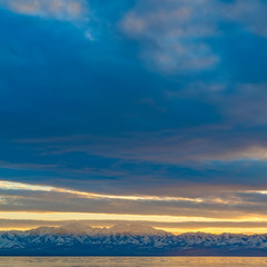 Square frame Scenic panorama of a lake and snow capped mountain under a striking cloudy sky