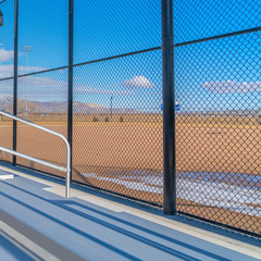 Square frame Sunlit bleachers overlooking a vast sports field on the other side of the fence