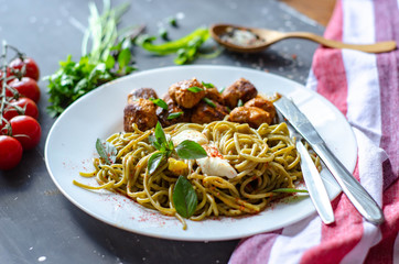 Spinach spaghetti with meatballs and egg. Green tasty pasta served with cherry tomatoes and basil