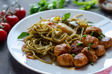 Spinach spaghetti with meatballs and egg. Green tasty pasta served with cherry tomatoes and basil