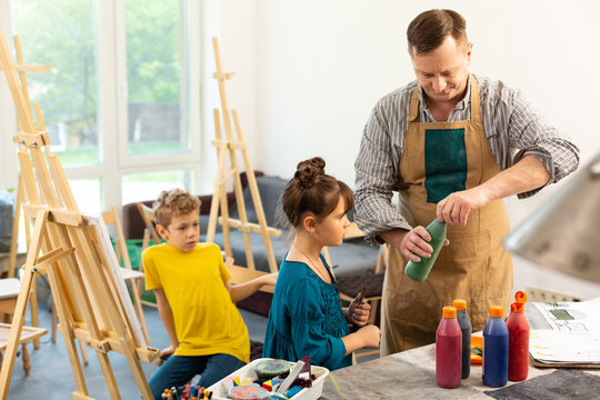 Art teacher wearing uniform opening paints for children