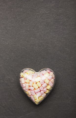Marshmallow in a container in the form of a heart on a stone background. Sweets for Valentine's Day.