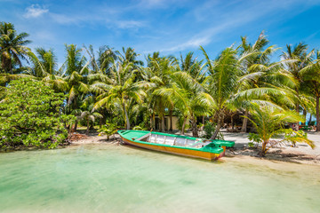 Obraz na płótnie Canvas Beautiful tropical destination with palm trees and an empty boat docked on the white sandy beach of Bora Bora Island, French Polynesia.