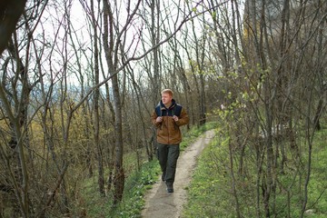 Obraz premium Redhead man in a brown-and-blue windbreaker with backpack walks in the woods in the Crimea in the early spring toward the camera. Travel, adventure, hiking and motivation concept.