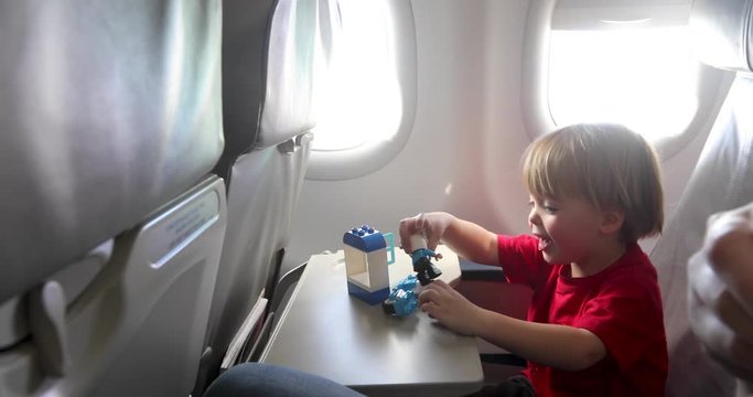 Little boy smiling and playing with toys while sitting near aircraft window during flight