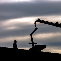 Square Man standing on the roof silhouetted against a bright sky with gray clouds