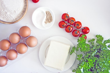 Ingredients for pizza, tomatoes, cheese, flour, eggs, yeast on a white background, flat lay, copy space