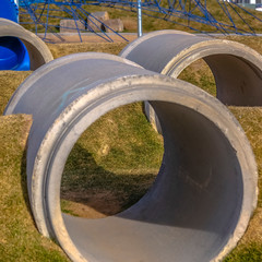 Square frame Concrete tunnels between grassy mounds at a playground viewed ona sunny day