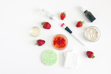 Homemade strawberry facial mask. Next to fresh strawberries, cotton napkins, brush, cosmetic, sponge and other ingredients. Top view, white background. The concept of natural skin care