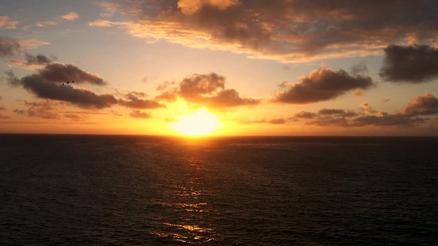 Aerial view of sunrise over ocean with birds flying and clouds moving