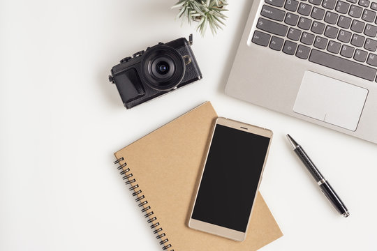 Creative flat lay photo of workspace desk with laptop, blank copy space smartphone and camera on white table background. Mockup blank space smartphone for travelling planning concept, minimal design.