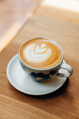 Latte art heart shape served in ceramic cup on wooden table.