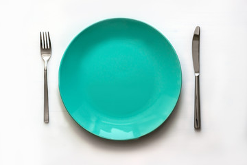 Empty clean green plate and stainless knife and fork isolated on white background. Top view