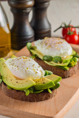 Avocado toast, cherry tomato and poached eggs on wooden background. Breakfast with vegetarian food, healthy diet concept.