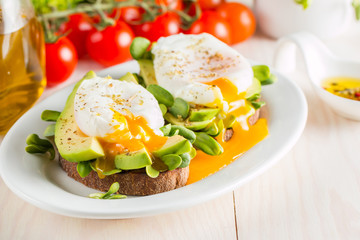 Avocado toast, cherry tomato and poached eggs on wooden background. Breakfast with vegetarian food, healthy diet concept.