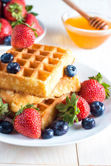 Fresh homemade food of berry Belgian waffles with honey, chocolate, strawberry, blueberry, maple syrup and cream. Healthy dessert breakfast concept with juice