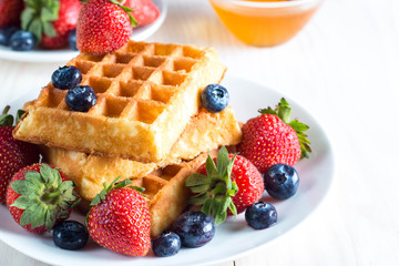 Fresh homemade food of berry Belgian waffles with honey, chocolate, strawberry, blueberry, maple syrup and cream. Healthy dessert breakfast concept with juice