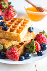 Fresh homemade food of berry Belgian waffles with honey, chocolate, strawberry, blueberry, maple syrup and cream. Healthy dessert breakfast concept with juice