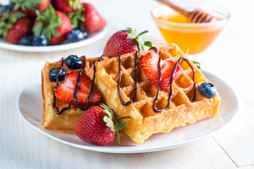 Fresh homemade food of berry Belgian waffles with honey, chocolate, strawberry, blueberry, maple syrup and cream. Healthy dessert breakfast concept with juice