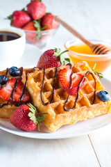 Fresh homemade food of berry Belgian waffles with honey, chocolate, strawberry, blueberry, maple syrup and cream. Healthy dessert breakfast concept with juice