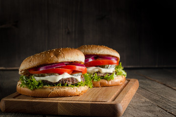 Home made hamburger with beef, onion, tomato, lettuce and cheese. Fresh burger close up on wooden rustic table with potato fries, beer and chips. Cheeseburger.