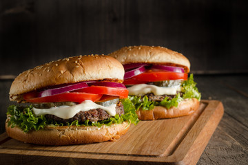 Home made hamburger with beef, onion, tomato, lettuce and cheese. Fresh burger close up on wooden rustic table with potato fries, beer and chips. Cheeseburger.