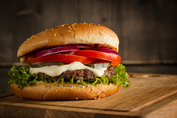 Home made hamburger with beef, onion, tomato, lettuce and cheese. Fresh burger close up on wooden rustic table with potato fries, beer and chips. Cheeseburger.