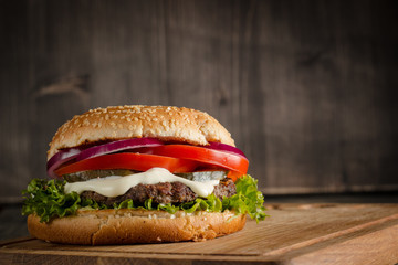 Home made hamburger with beef, onion, tomato, lettuce and cheese. Fresh burger close up on wooden rustic table with potato fries, beer and chips. Cheeseburger.