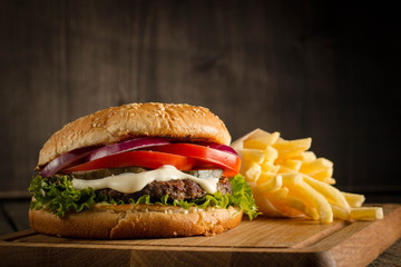 Home made hamburger with beef, onion, tomato, lettuce and cheese. Fresh burger close up on wooden rustic table with potato fries, beer and chips. Cheeseburger.