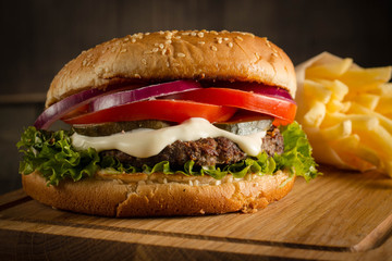 Home made hamburger with beef, onion, tomato, lettuce and cheese. Fresh burger close up on wooden rustic table with potato fries, beer and chips. Cheeseburger.
