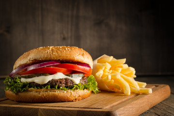 Home made hamburger with beef, onion, tomato, lettuce and cheese. Fresh burger close up on wooden rustic table with potato fries, beer and chips. Cheeseburger.