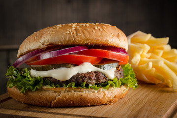 Home made hamburger with beef, onion, tomato, lettuce and cheese. Fresh burger close up on wooden rustic table with potato fries, beer and chips. Cheeseburger.