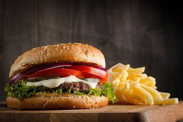 Home made hamburger with beef, onion, tomato, lettuce and cheese. Fresh burger close up on wooden rustic table with potato fries, beer and chips. Cheeseburger.