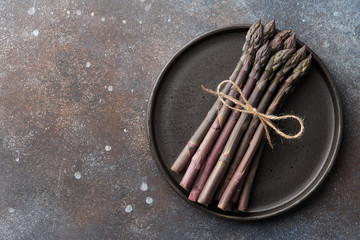Bunch of purple asparagus in plate on textured rusty background