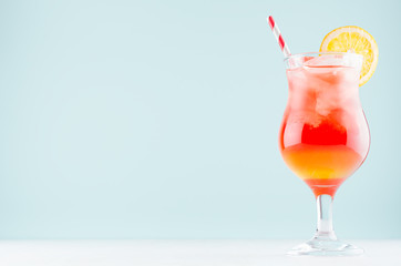 Summer cold alcohol striped cocktail with oranges juice, straw, ice cubes in luxury glass on pastel blue background, copy space.