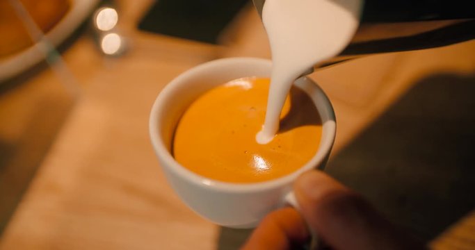 Close up hand of barista pouring latte art with espresso and milk froth in white hot ceramic cup